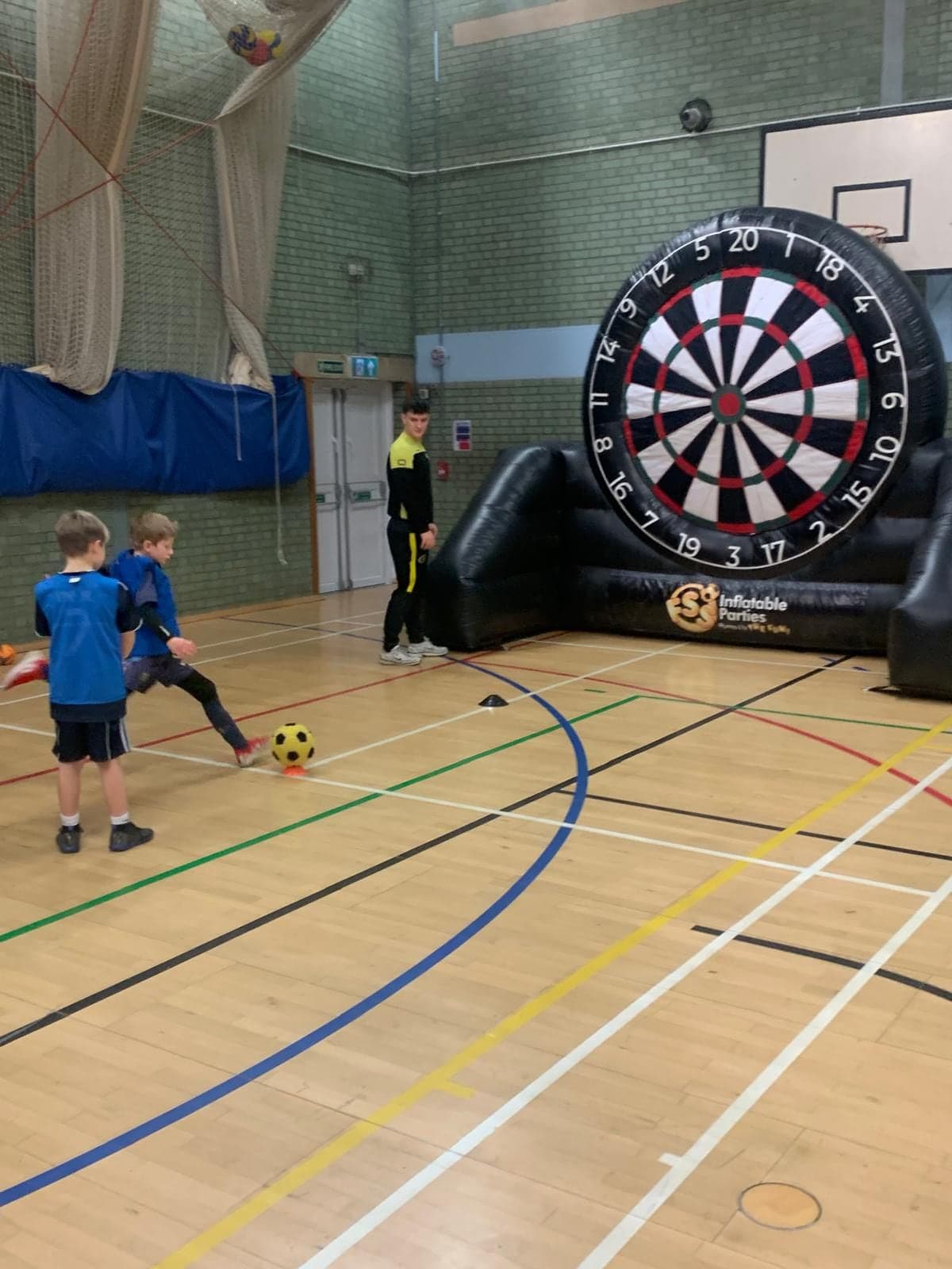 A child kicking a ball at the inflatable football darts board while a coach watches
