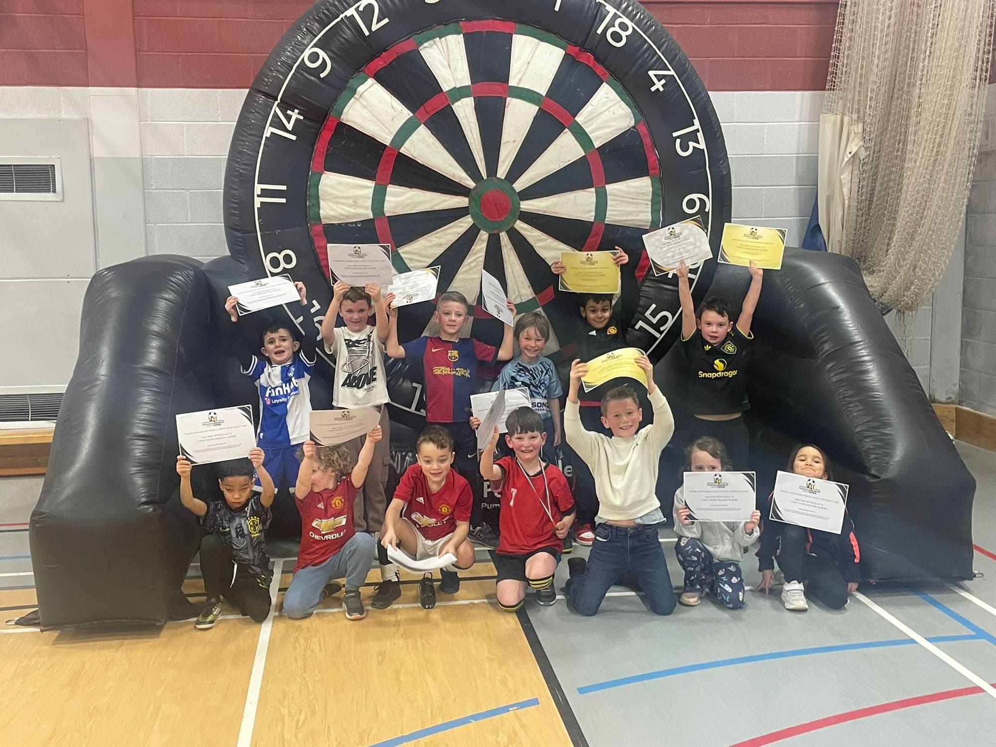 A party group holding up their certificates in front of the football darts board