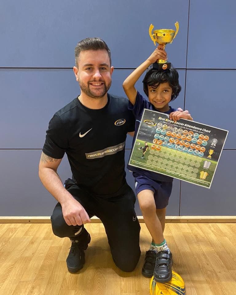 A young footballer holding up a trophy next to coach Joe